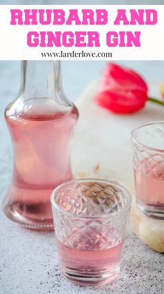 two glasses filled with pink liquid sitting on top of a table next to a bottle