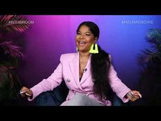 a woman with long black hair sitting in a chair and smiling at the camera while wearing neon earrings