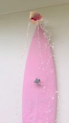 a pink surfboard being sprayed with water by a faucet on the wall