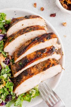 a white plate topped with sliced chicken next to a salad