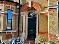 a brick building with a black door and window frames on the front porch, surrounded by potted plants