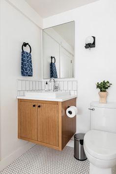 a white toilet sitting next to a wooden cabinet in a bathroom under a large mirror