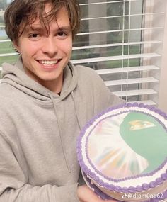 a young man holding a cake in front of a window