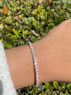 a woman's arm with a bracelet on top of it and bushes in the background