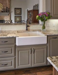 a white kitchen sink sitting under a window next to a counter top with flowers in it