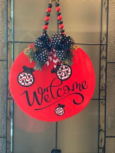 a red welcome sign hanging from the side of a building with ladybugs on it