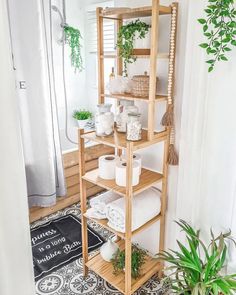 a wooden shelf filled with white towels and plants next to a potted houseplant