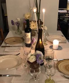 a table set with wine bottles, glasses and plates for two people to eat together