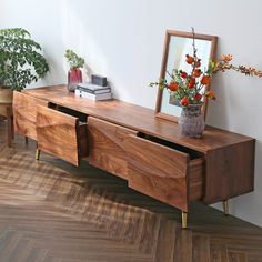 a vase with flowers on top of a wooden table next to a mirror and potted plants