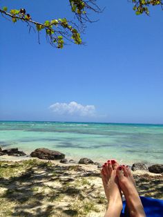 a person laying on the beach with their feet up in the sand and water behind them