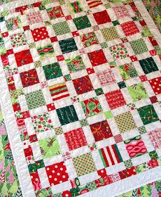 a red and green quilted christmas themed table topper on a white bed sheet