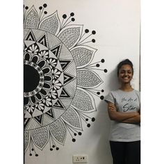 a woman standing next to a wall with a black and white design on it