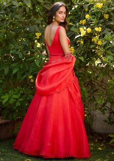 a woman in a red dress standing next to some bushes