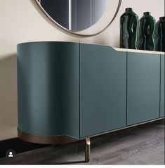 a sideboard with two green vases and a round mirror on the wall above it