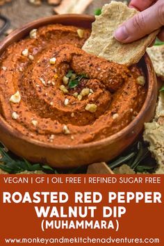 a hand dipping a tortilla chip into a bowl of roasted red pepper walnut dip