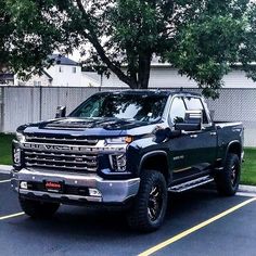 a large black truck parked in a parking lot next to a tree and fenced area