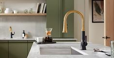 a kitchen with green cabinets and gold faucet on the counter top next to a sink