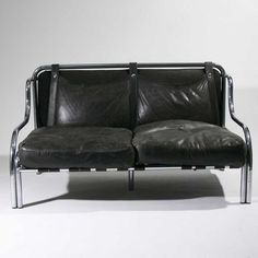 a black leather couch sitting on top of a white floor next to a metal frame