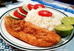 a white plate topped with fish and rice next to sliced cucumbers, tomatoes and limes