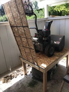 a lawn mower sitting on top of a piece of plywood next to a fence