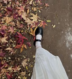 a person's feet in black and white shoes on the ground with autumn leaves