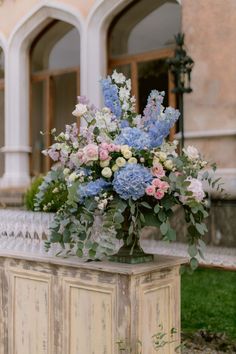 a vase filled with blue and pink flowers sitting on top of a wooden table in front of a building