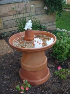 a bird bath in the middle of a flower bed with rocks and gravel around it