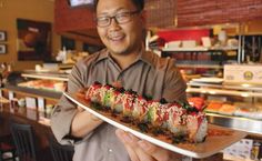 a man holding a plate with sushi on it in front of a restaurant counter