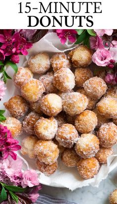 a white plate topped with donuts covered in powdered sugar next to pink flowers