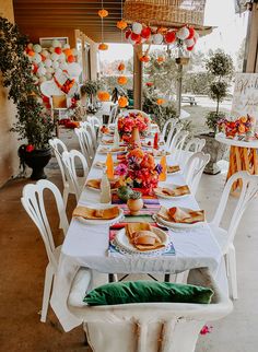 a long table set up for a party with orange and white balloons hanging from the ceiling