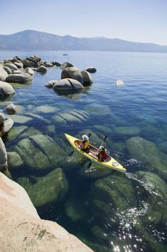 a person in a kayak paddling on the water near some rocks and boulders