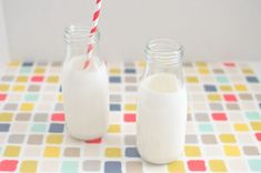 two glass jars filled with milk sitting on top of a colorful table cloth next to a red and white striped straw