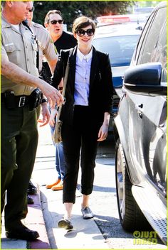 a woman in black pants and white shirt standing next to a police officer with her hand on