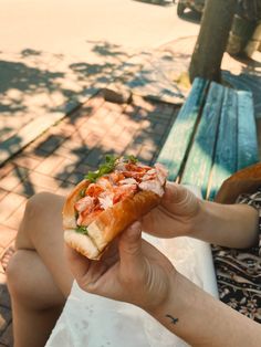 a person sitting on a bench holding a sandwich in their hand and eating it with both hands