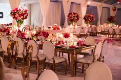 the tables are set with white chairs and red centerpieces on top of them