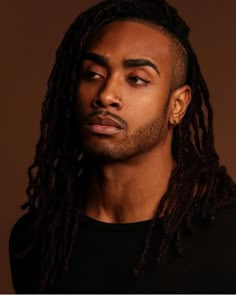 a man with long dreadlocks looks into the distance while wearing a black shirt