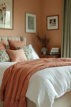 a bedroom with peach walls and white bedding in the corner, along with two framed pictures on the wall