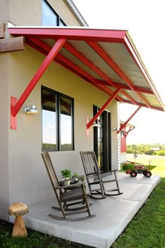 two rocking chairs sitting on top of a cement slab under a red awning next to a white house