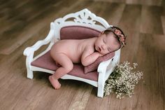 a baby sleeping on a pink chair with flowers in it's hair and wearing a headband