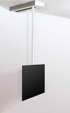 a black square hanging from the ceiling in an empty room next to a white wall