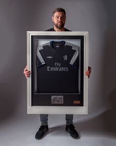 a man holding up a framed soccer shirt with the name emirates printed on it in front of his face