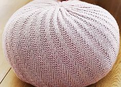 a pink knitted poufce sitting on top of a wooden floor next to a vase