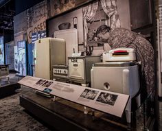 an old fashioned refrigerator and other appliances are on display in a museum exhibit room with black and white photos