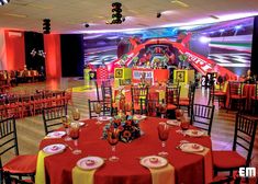 a banquet hall set up with red and yellow tablecloths, gold plates and silverware