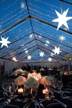 a large tent with tables and chairs under the stars on the ceiling is lit up at night