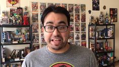 a man with glasses making a surprised face in front of comic books on the wall