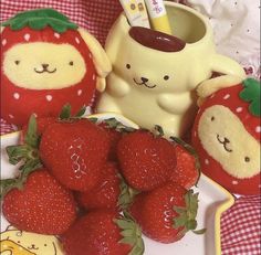 some strawberries are sitting on a plate with a cup and two teddy bears in the background