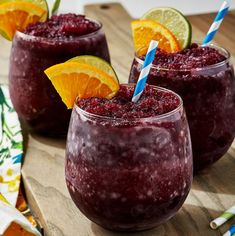 two glasses filled with smoothie and garnished with orange slices on a wooden cutting board