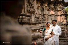 a man and woman standing next to each other in front of a stone structure with carvings on it