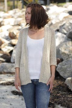 a woman standing in front of rocks wearing a white top and blue jeans with her hands in her pockets